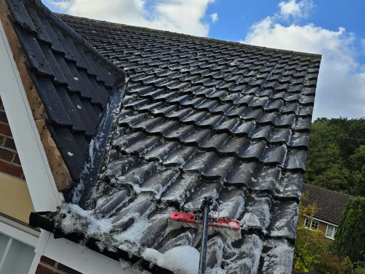Biocide solution foaming across roof tiles and into the gutter during a soft wash roof clean