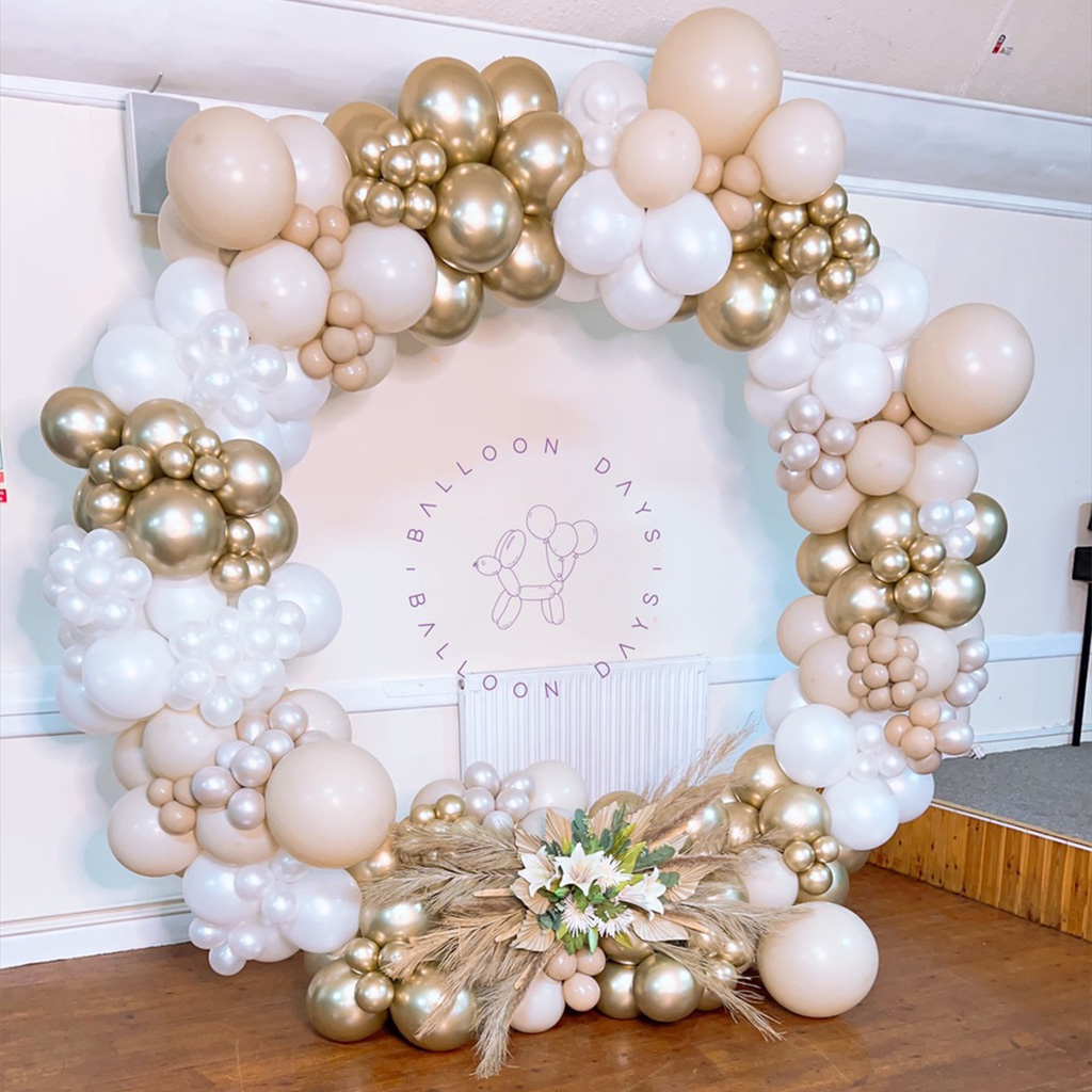 Elegant nude and gold circular balloon hoop with pampas grass against a hall backdrop