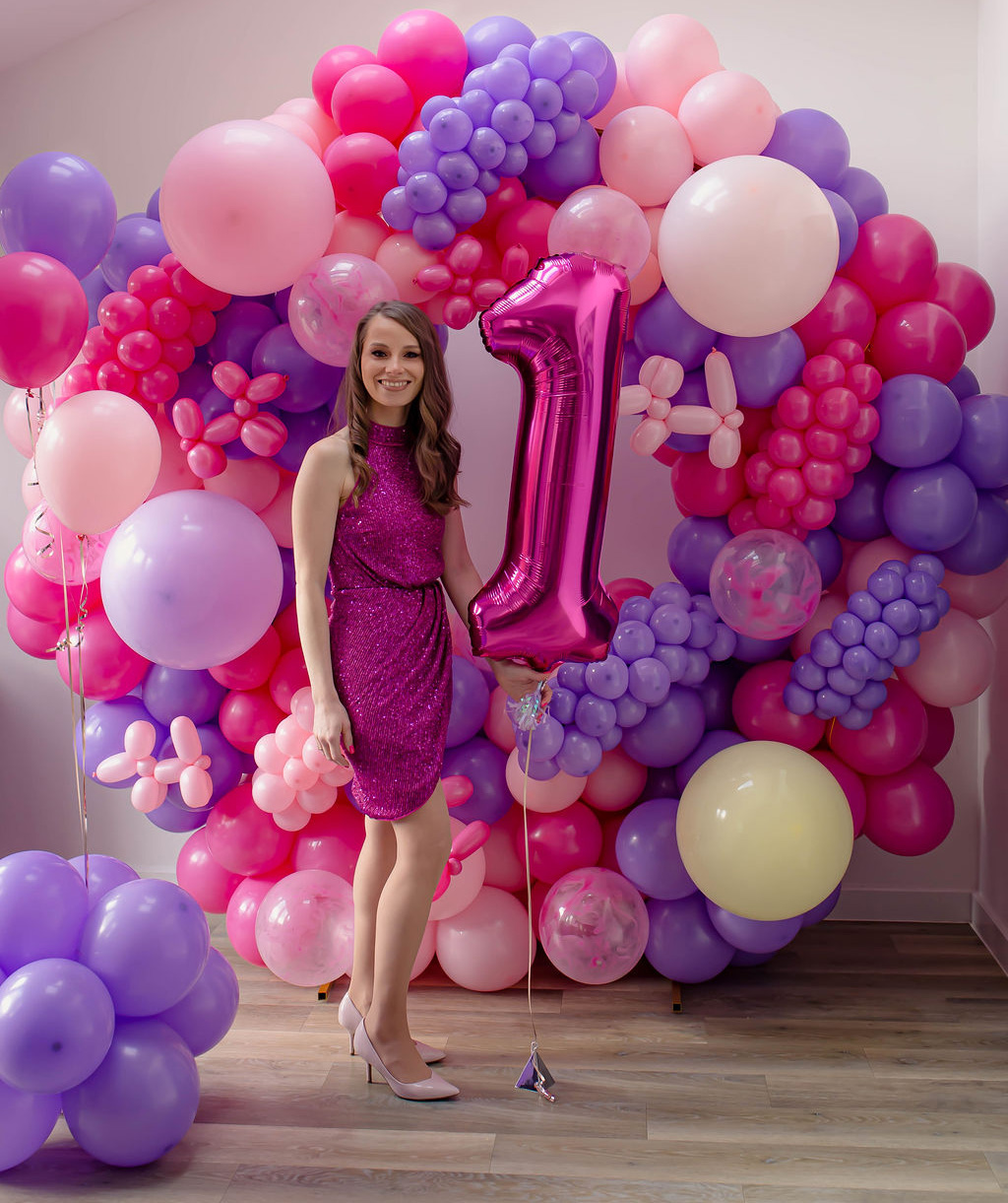 Marta, founder of Balloon Days, smiling in a sparkling magenta dress in front of one of her handmade pink and purple balloon garlands