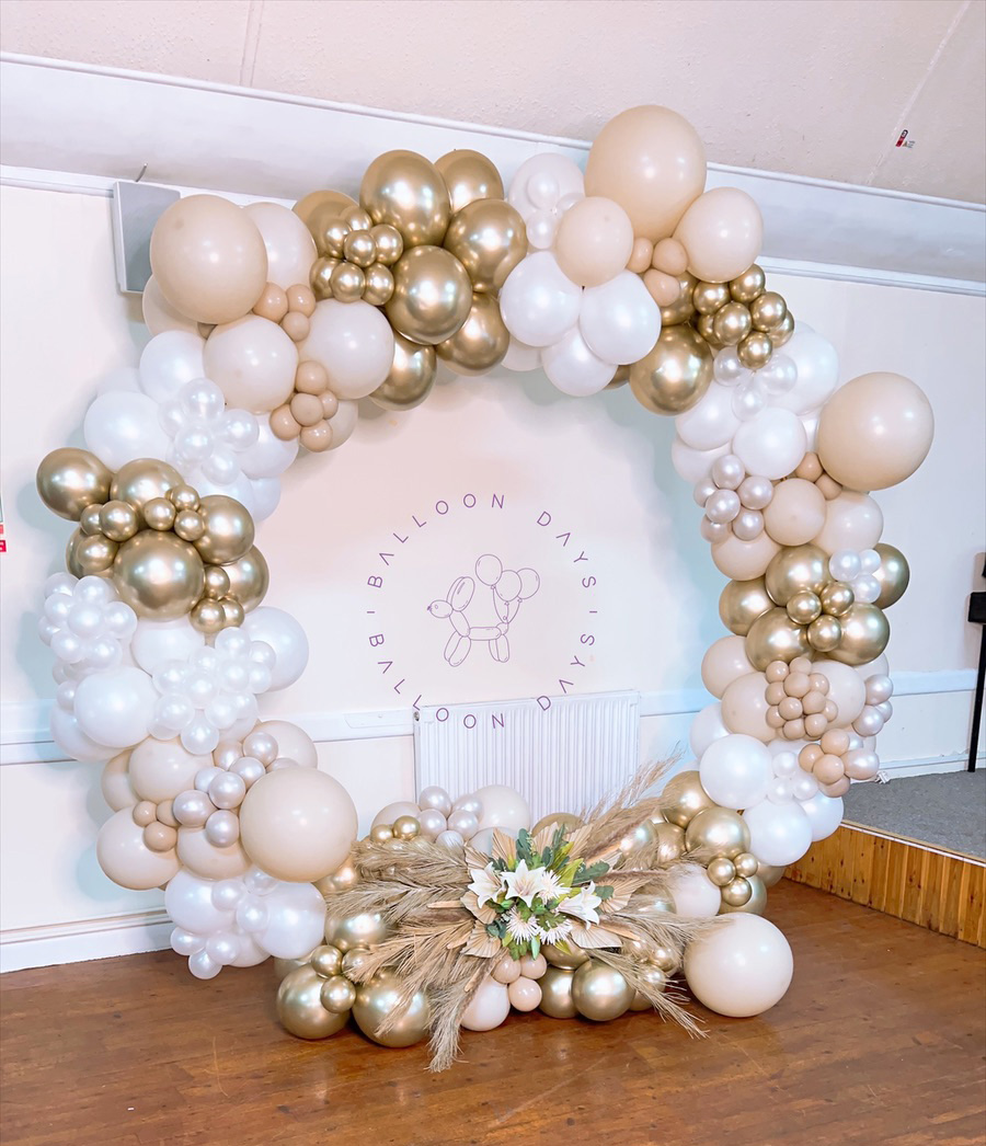 An elegant circular balloon hoop in white, nude and chrome gold dressed with pampas grass and lilies for a wedding