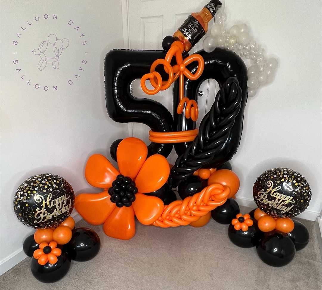 A dramatic black and orange fiftieth birthday balloon display with a large number fifty, balloon flowers and a whisky bottle detail
