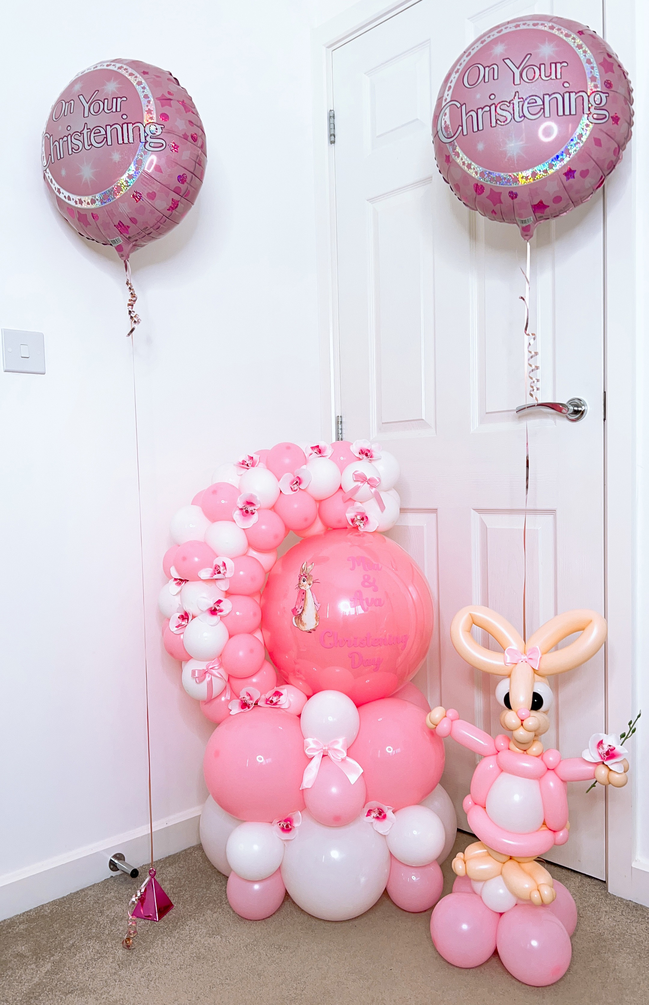 A soft pink christening balloon display with a handmade balloon rabbit and a personalised bubble balloon
