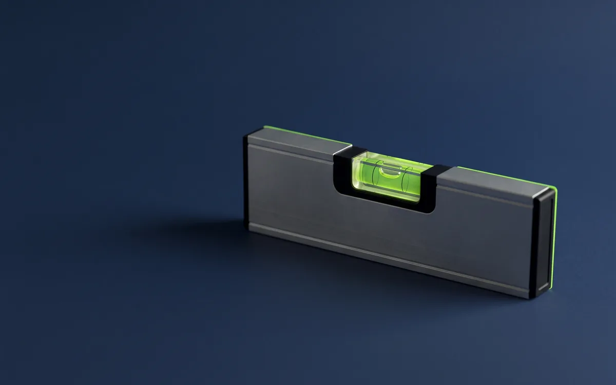 Illustration: a short aluminium spirit level standing on its edge on a navy backdrop, its vial glowing lime and the bubble slightly off-centre.