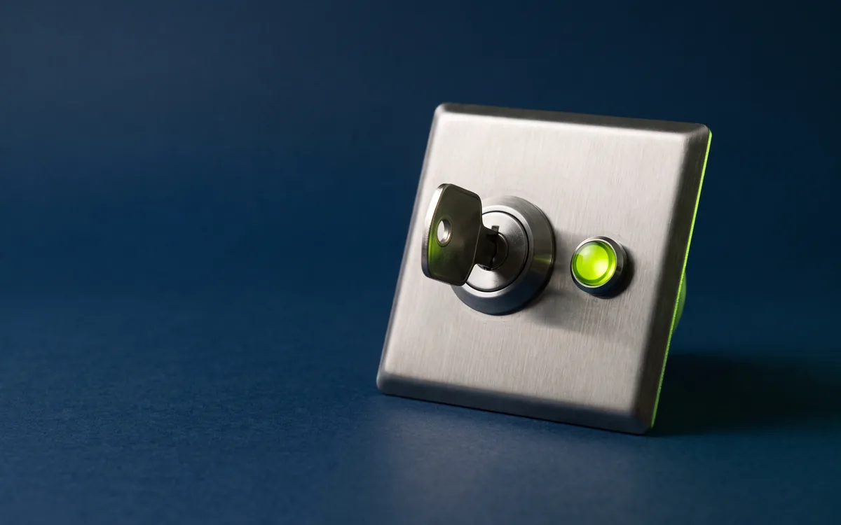 Illustration: a brushed steel key switch with a key inserted and a lime indicator lamp lit beside it, on a navy backdrop.