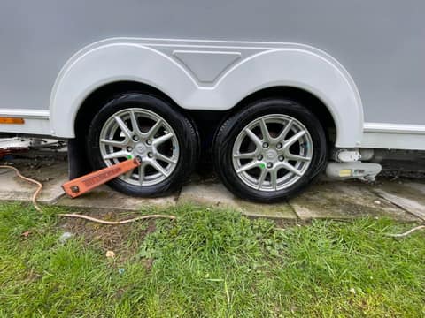 The twin axle wheels of a caravan, alloys cleaned and tyres dressed, with a wheel clamp fitted.