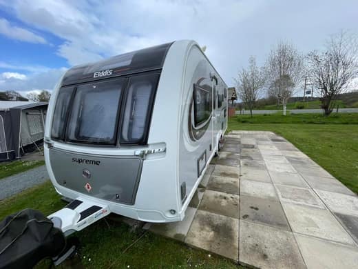 An Elddis Supreme touring caravan after cleaning, photographed from the front corner on a paved pitch.
