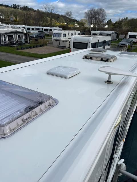 A cleaned caravan roof at a storage park, with caravans and a wooded hillside behind.