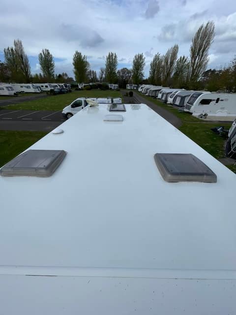 A cleaned caravan roof with two rooflights, a storage park and a line of poplars behind.