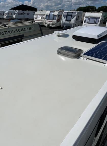 A caravan roof after cleaning, the white surface even and bright, with a solar panel and a Truma unit fitted, and the Eastment's Caraclean van parked alongside in the storage compound.