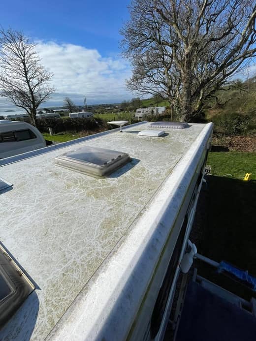 A caravan roof before cleaning, the surface mottled with weathered staining around the rooflight.