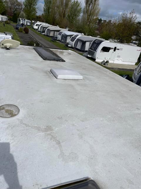 A weathered caravan roof, grey and streaked, with a row of stored caravans running away behind it.