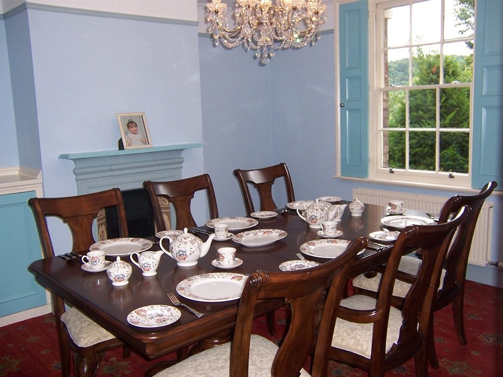The dining room by day, the mahogany table laid with patterned china for breakfast beneath blue walls and a gorge-view sash window