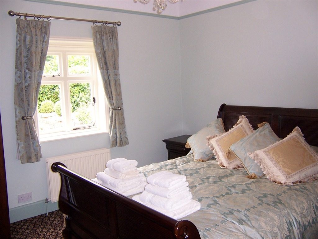A pale-blue bedroom with a dark mahogany sleigh bed, gold damask bedspread, folded white towels and a small crystal chandelier