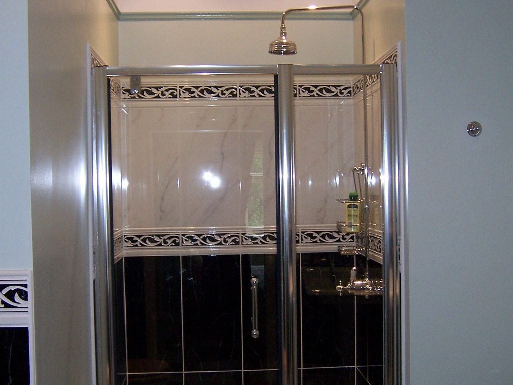 A bedroom seen past its en-suite, with a black marble basin and chrome fittings in the foreground and a damask bed and chandelier through a green panelled door