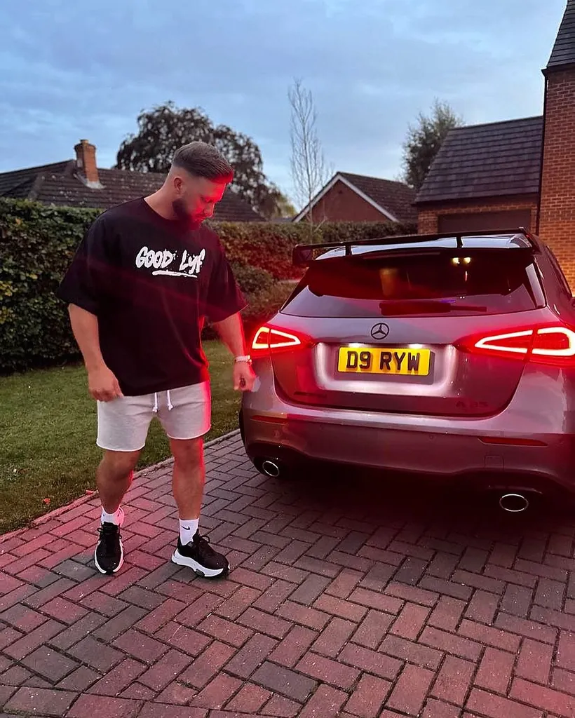 A black GoodLyf tee worn on a driveway beside a parked car.