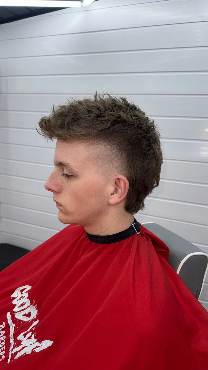 Textured length on top over a tight fade, side profile, client in a red cape