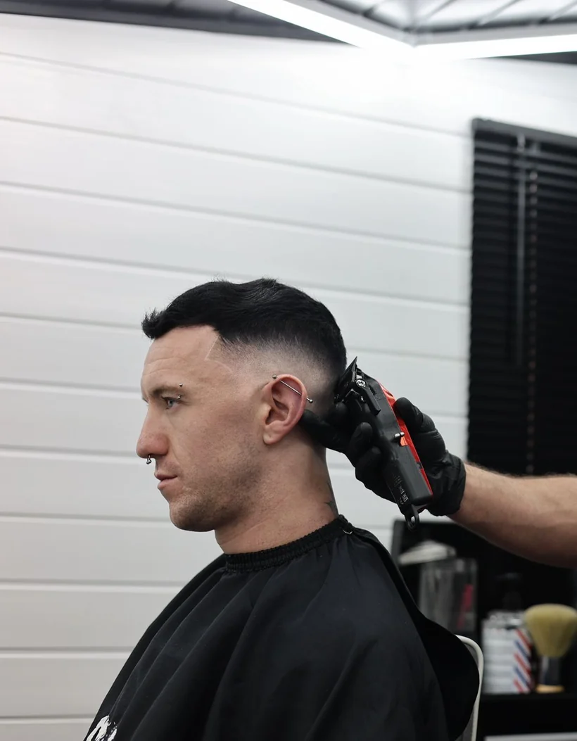 Clipper work through a skin fade, seen in profile, client in a black cape