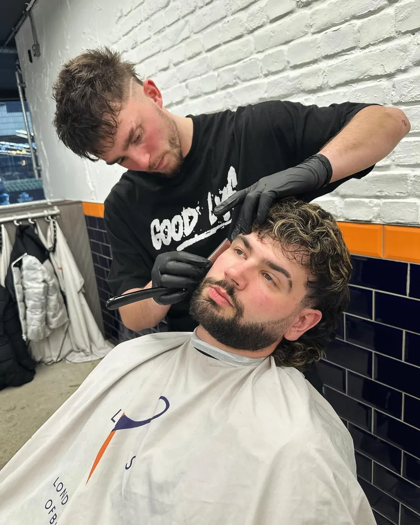 A GoodLyf barber cutting a client at the white brick wall