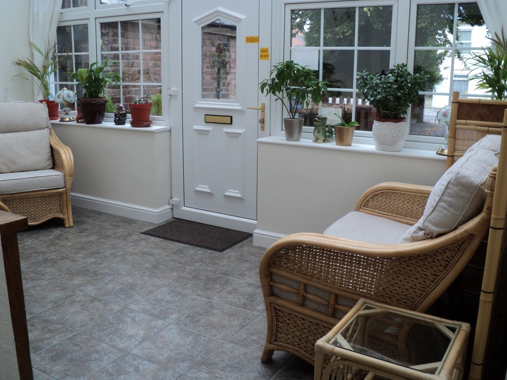 Grove House's conservatory entrance: cane armchairs, potted greenery along the windowsills and the white panelled front door