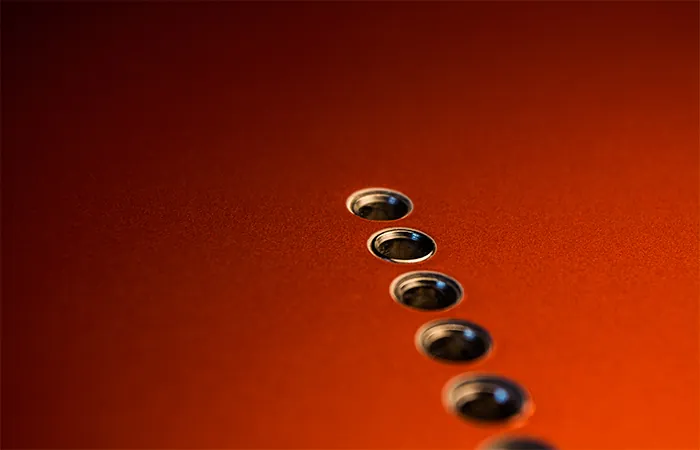 A close view of a copper metallic guitar body showing six string ferrules set into the wood for through body stringing
