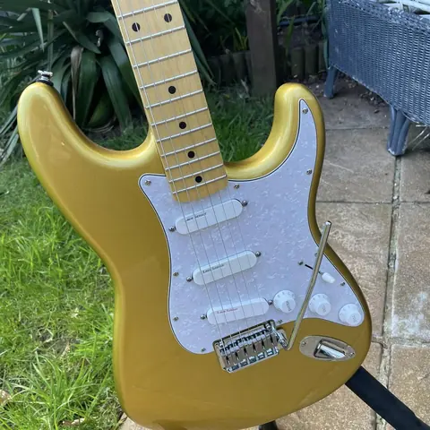A gold finish J. Davey Stratocaster with a white pearl pickguard, three Lace Sensor pickups and a maple neck, photographed outdoors