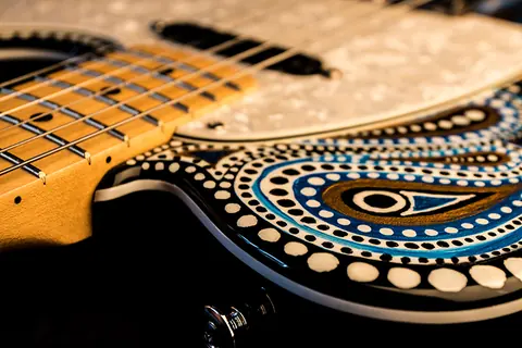 Close detail of the hand painted artwork, rows of white dots and blue teardrop shapes, beside the maple fingerboard
