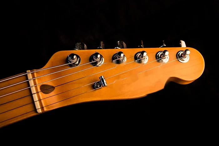 A maple Telecaster headstock with six chrome tuners and the strings running over the nut, photographed against black