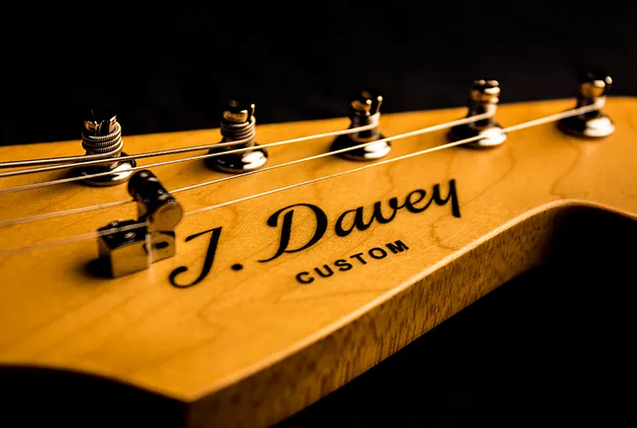 The J. Davey Custom decal side lit on a maple Stratocaster headstock, chrome tuners catching the light