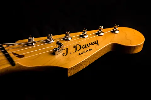 A maple Stratocaster headstock carrying the J. Davey Custom script decal and six chrome tuners