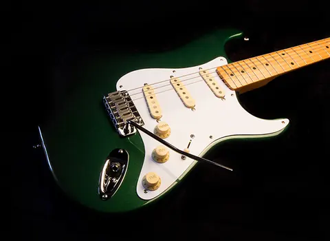 A metallic racing green J. Davey Stratocaster with a white pickguard, cream knobs and maple neck, photographed on black