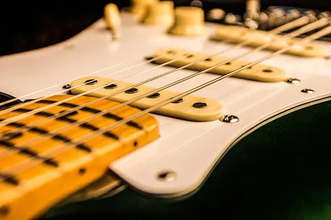 The three cream pickups of the racing green Stratocaster seen from the bridge, maple fingerboard beyond