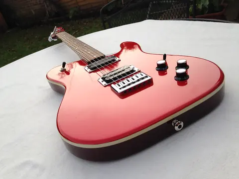 The matte red J. Davey Showroom Series guitar at an angle on a white sheet