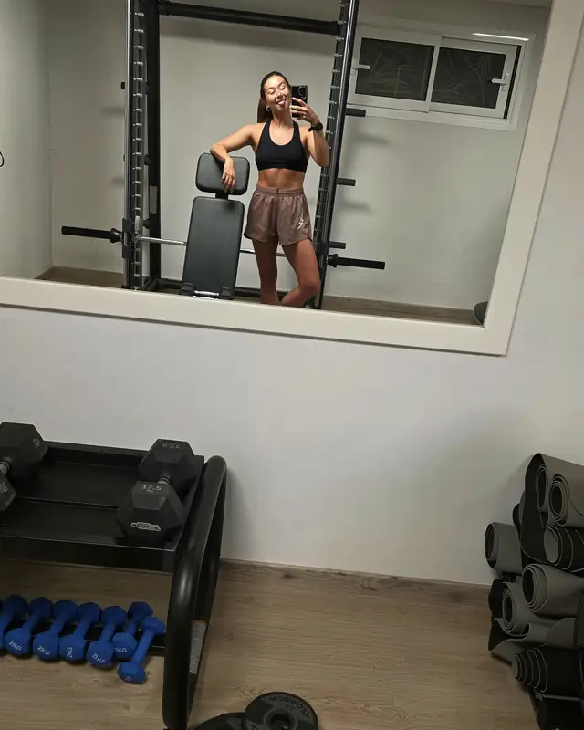 Lucy taking a mirror selfie in a home gym, phone in hand.