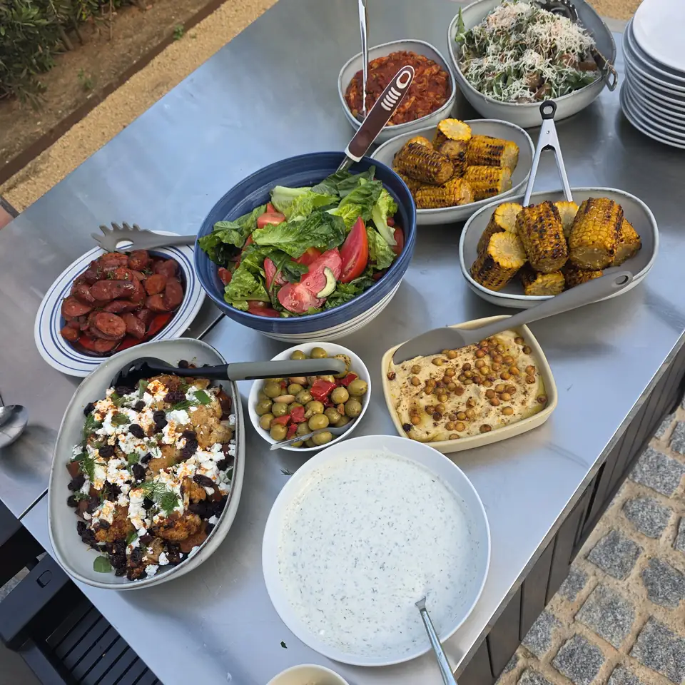 A table spread of retreat food: salads, roast potatoes, rice, dips and fresh tomatoes.