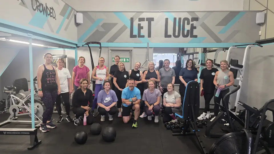 About twenty Let Luce clients posing together in the studio under the LET LUCE sign, with bikes and racks around them.