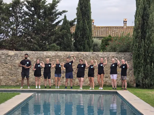 A Let Luce retreat group by a stone wall, flexing their arms, a pool in front of them.