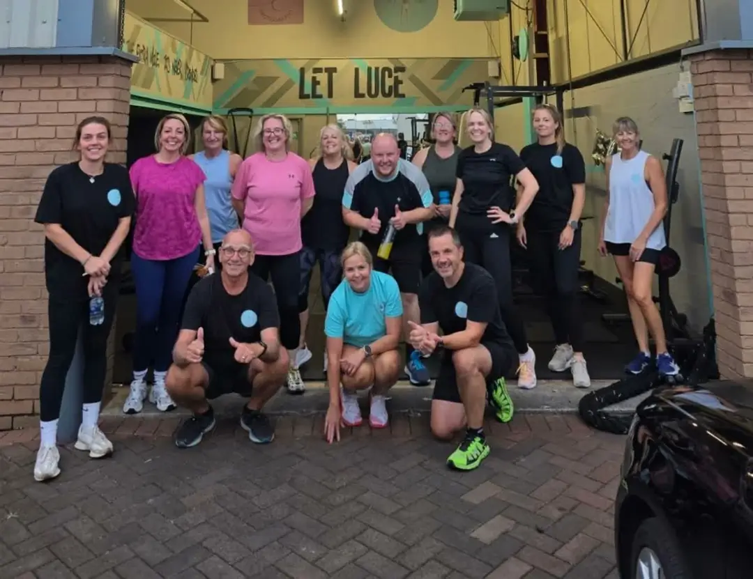 A group of clients and their coach smiling together in the doorway of Unit 49 under the Let Luce sign. (AI-animated from a real photo)