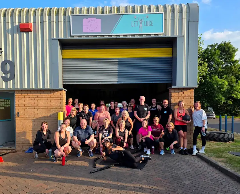 Lucy's crew gathered in front of the roller door of Unit 49, with the Let Luce sign above.