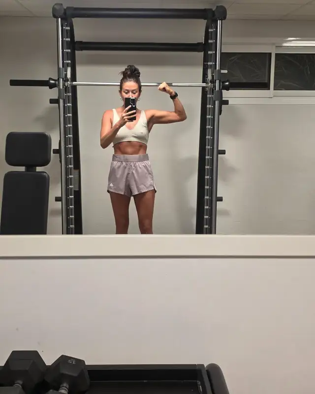 Lucy taking a mirror selfie beside a squat rack in her private gym
