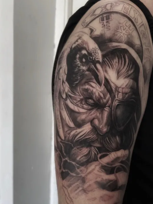 Winged creature beneath the moon in black and grey on the upper arm
