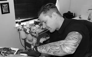 John Lewis tattooing at his station
