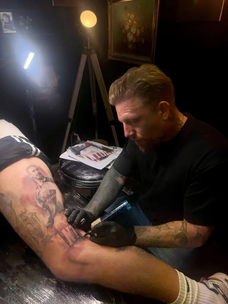 An artist working a colour portrait into a client's leg under the studio lamp