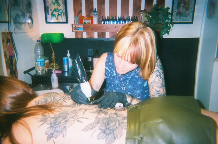 An artist shading a large floral back piece in the studio