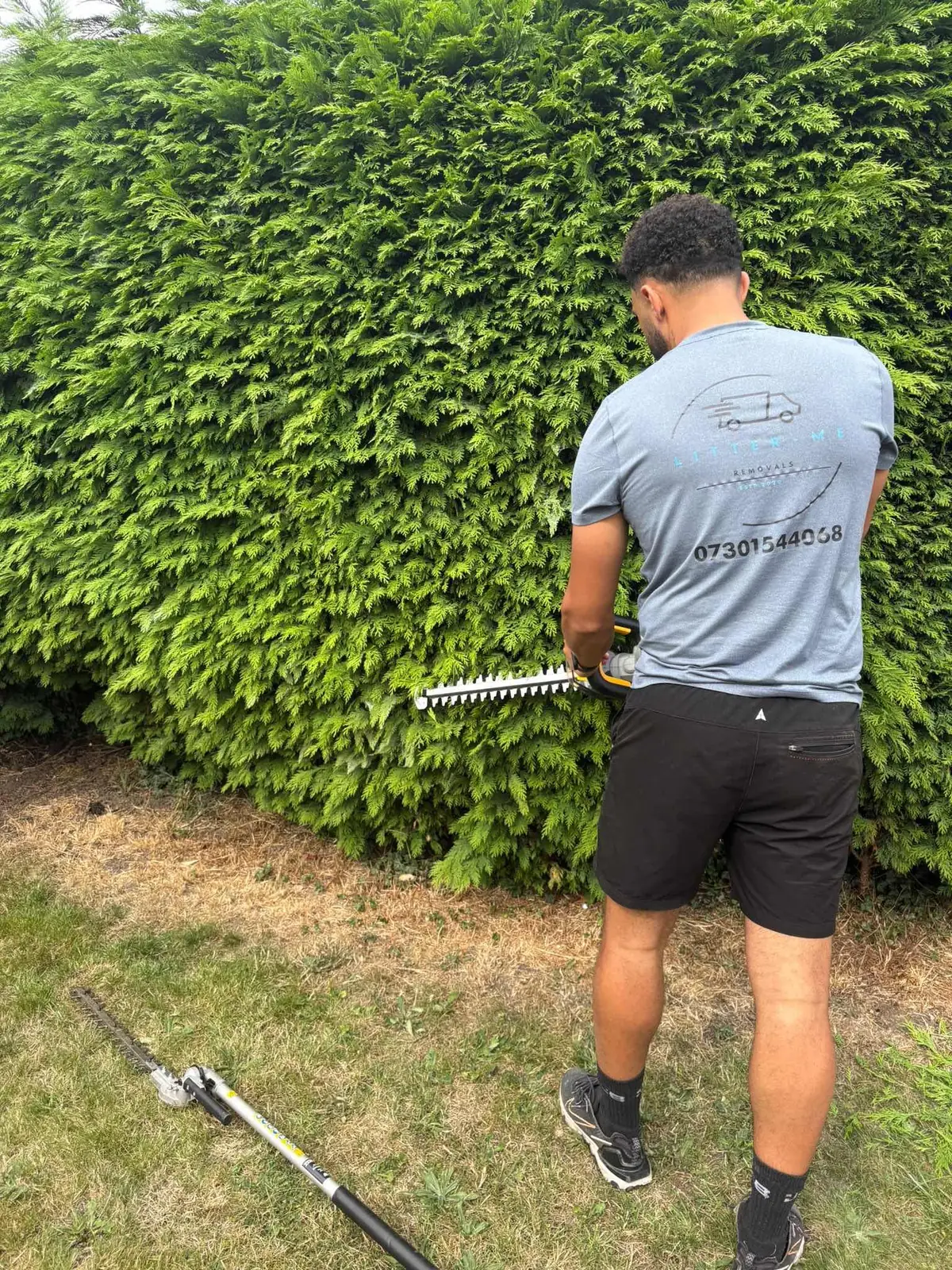 Litter Me Removals team member in branded uniform trimming a tall garden hedge