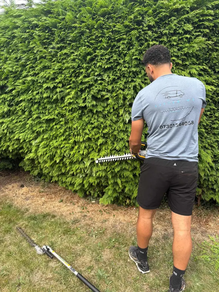 Litter Me Removals team member in branded uniform trimming a large garden hedge