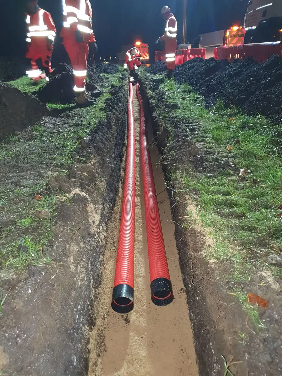 Twin power ducts laid in an open trench beside a carriageway at night