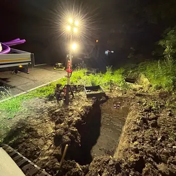 Night infrastructure works lit by a lighting tower beside a carriageway