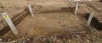 A wide shallow foundation pit dug out square, with labelled concrete posts standing at each corner.