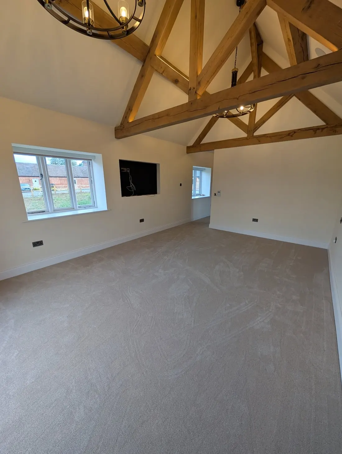 Beige carpet in a vaulted room with oak trusses, two windows and a wall mounted television.