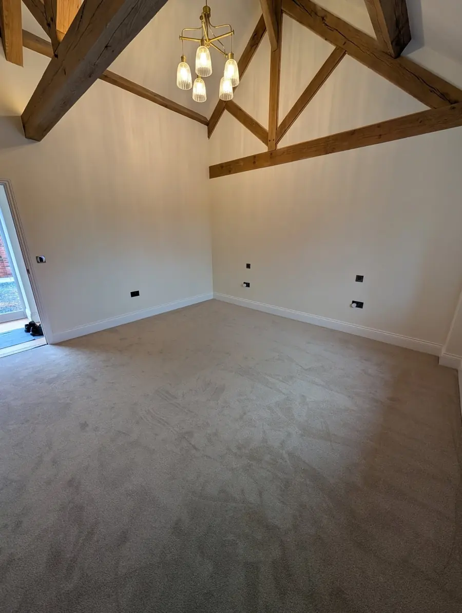Beige carpet in a bright vaulted room with oak trusses and a window to the garden.